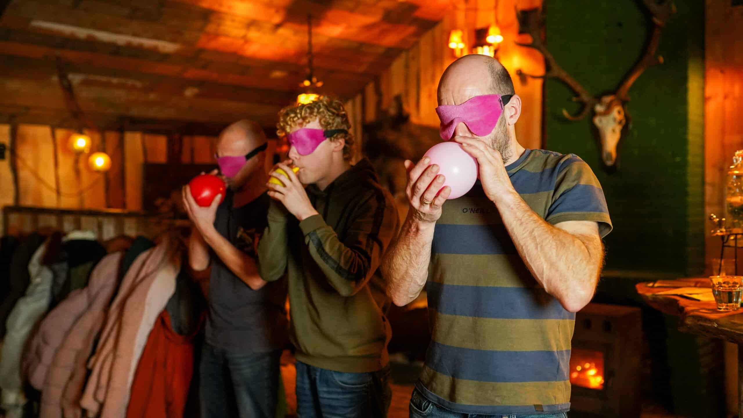 Drie mannen blazen ballonnen op tijdens een interactieve battle van de pubquiz